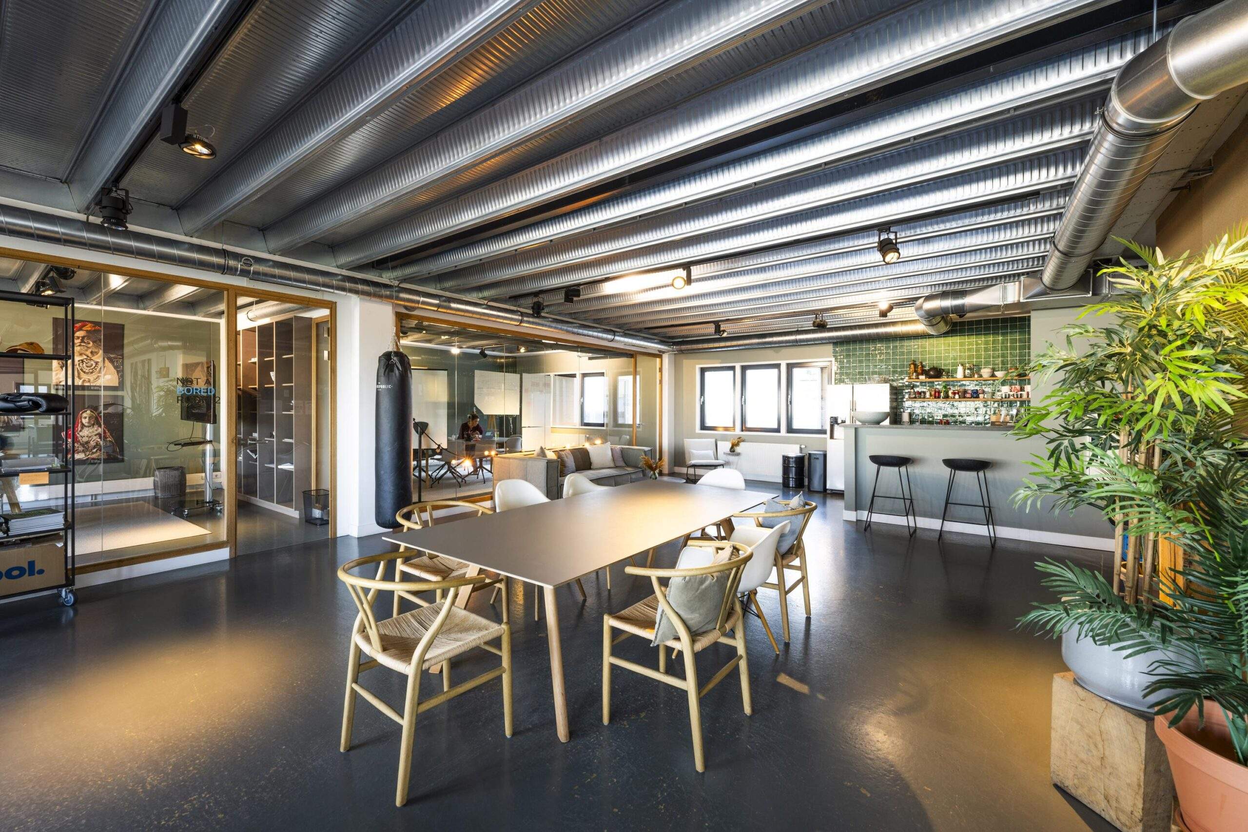 Modern office space on Helicopterstraat with a meeting table, lounge area, bar, and industrial-style ceiling.