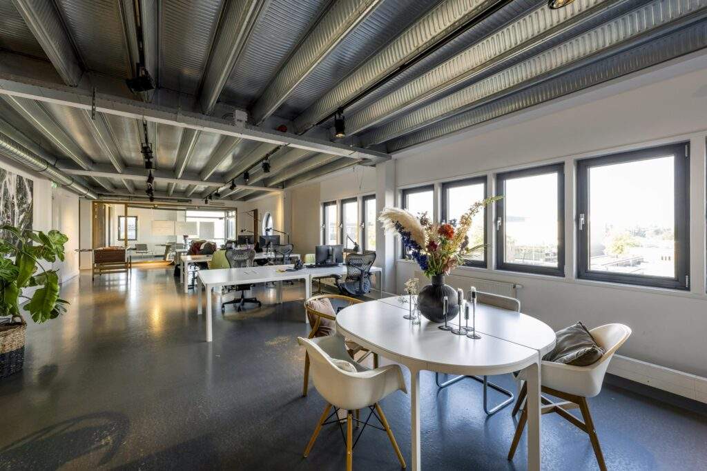 Modern open-plan office space on Helicopterstraat with large windows, industrial ceiling, and contemporary furniture.