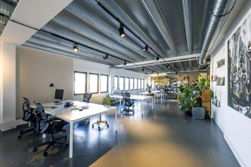 Modern open-plan office on Helicopterstraat with large windows, industrial ceiling, and minimalist white desks.