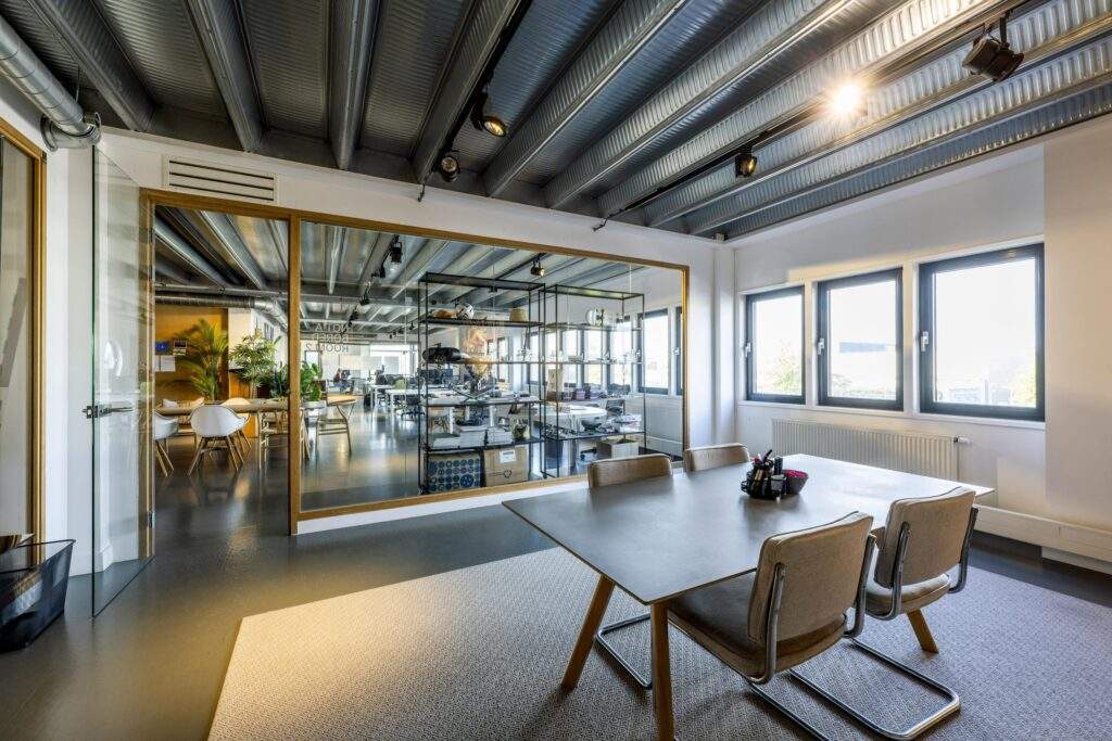 Modern meeting room with a large table, beige chairs, and glass wall overlooking an open office space on Helicopterstraat.