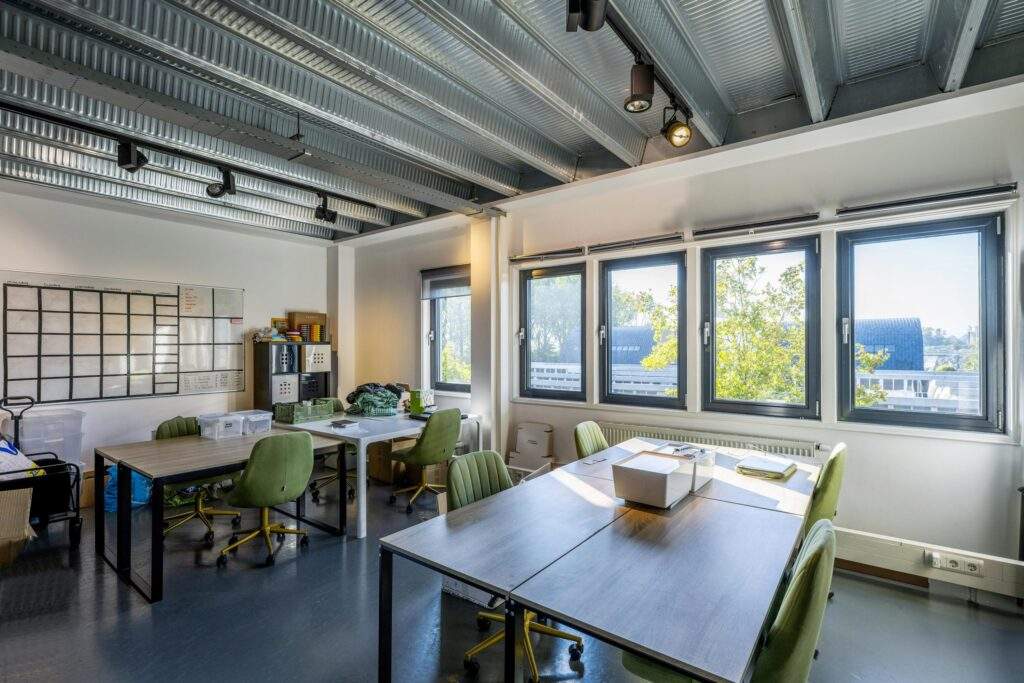 Modern office space on Helicopterstraat with green chairs, large windows, and exposed metal ceiling.