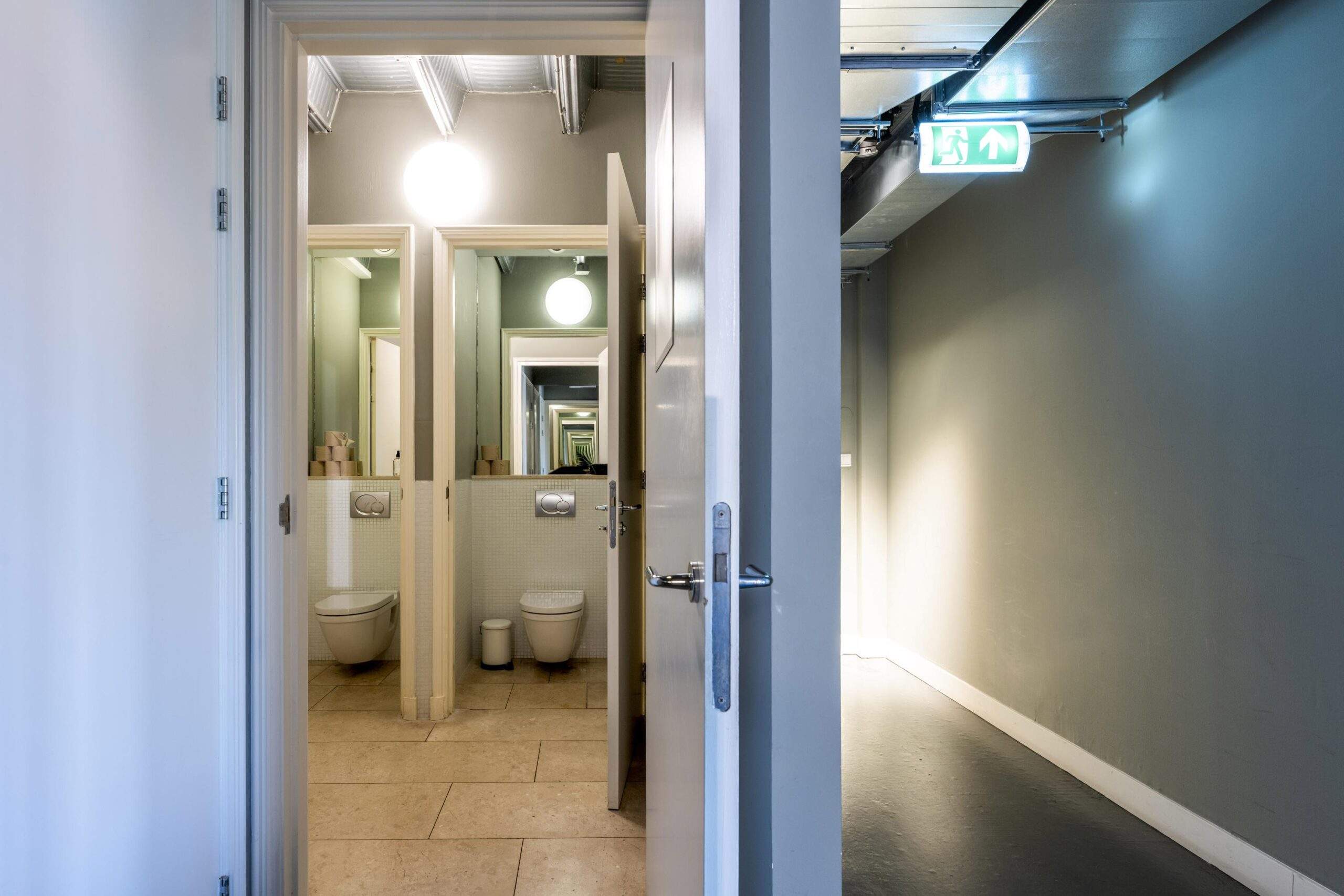 View through a door into a modern restroom area with mirrors creating an infinite reflection effect.