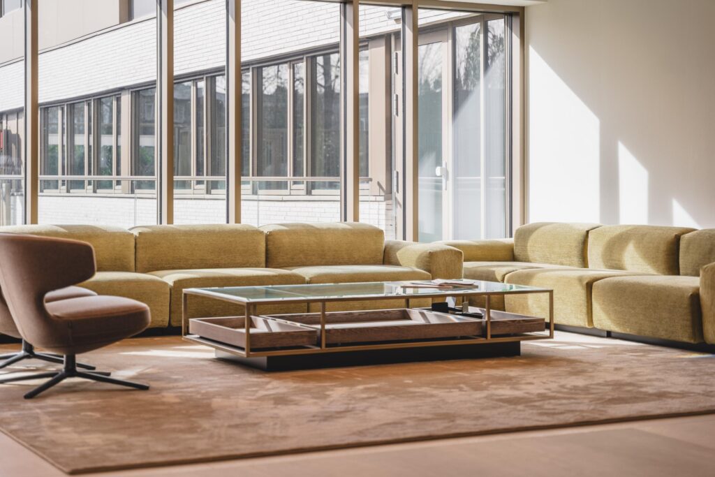 Moderne wachtruimte met een grote gele hoekbank, glazen salontafel en een bruine fauteuil bij Walborg.