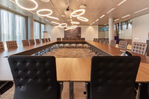 Vergaderruimte aan de Amstelveenseweg met een grote U-vormige tafel, leren stoelen en moderne ringvormige plafondverlichting.