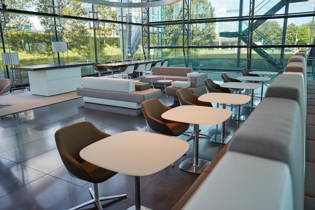 Moderne en licht ingerichte lounge met zitjes aan de Amstelveenseweg, omringd door glazen wanden en uitzicht op groen.