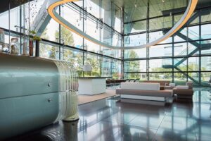Moderne en lichte ontvangsthal aan de Amstelveenseweg met glazen wanden, designmeubilair en een ronde lichtinstallatie aan het plafond.