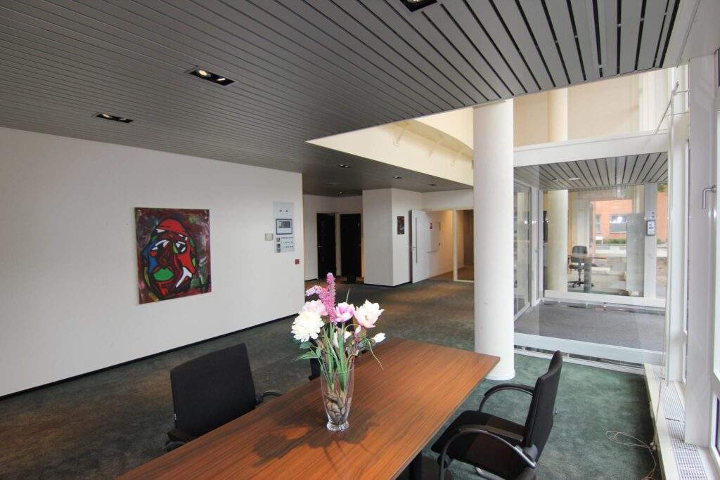 Modern office entrance with a wooden table, black chairs, a vase of flowers, abstract wall art, and glass doors.