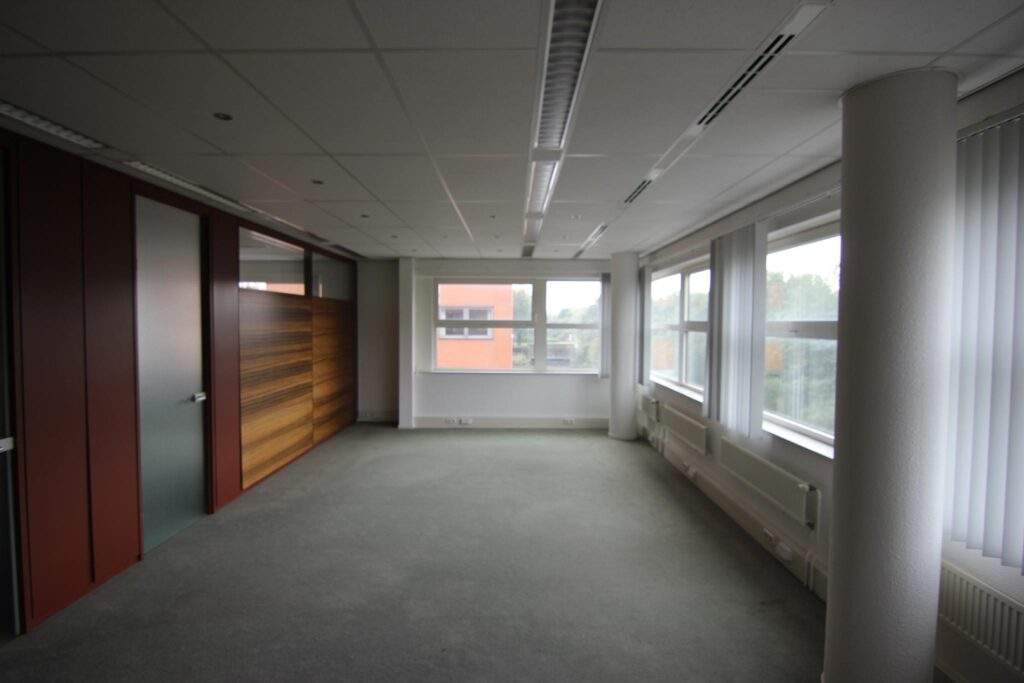 Empty office space with large windows, carpeted floor, and a wooden wall partition in the Entrada building.