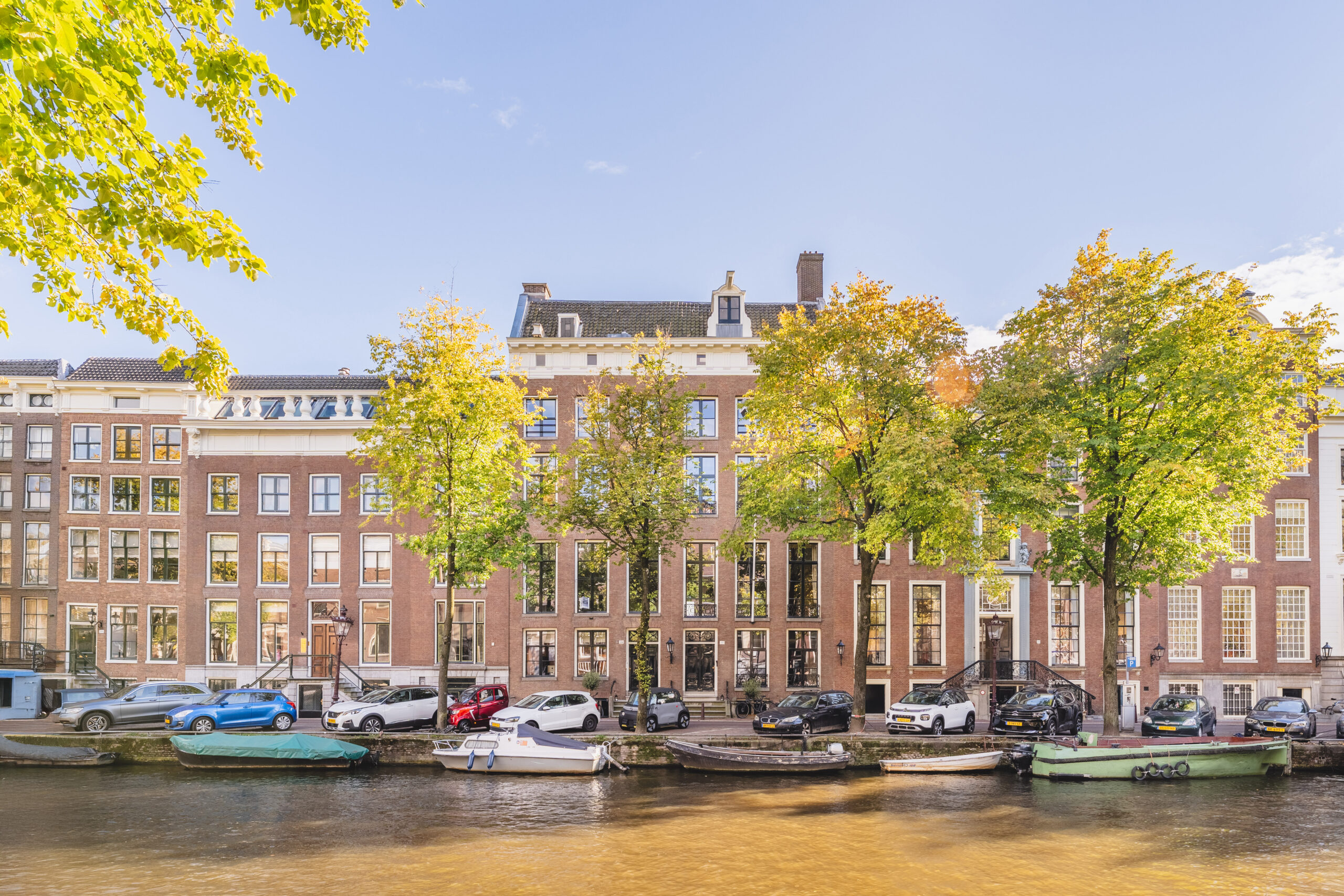 Canal-side view of historic brick buildings with parked cars and boats in Amsterdam.