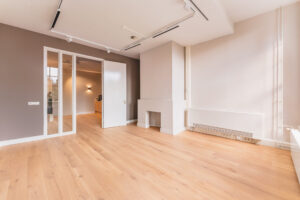 Bright, modern room with wooden flooring, a white radiator, and an open door leading to another space.