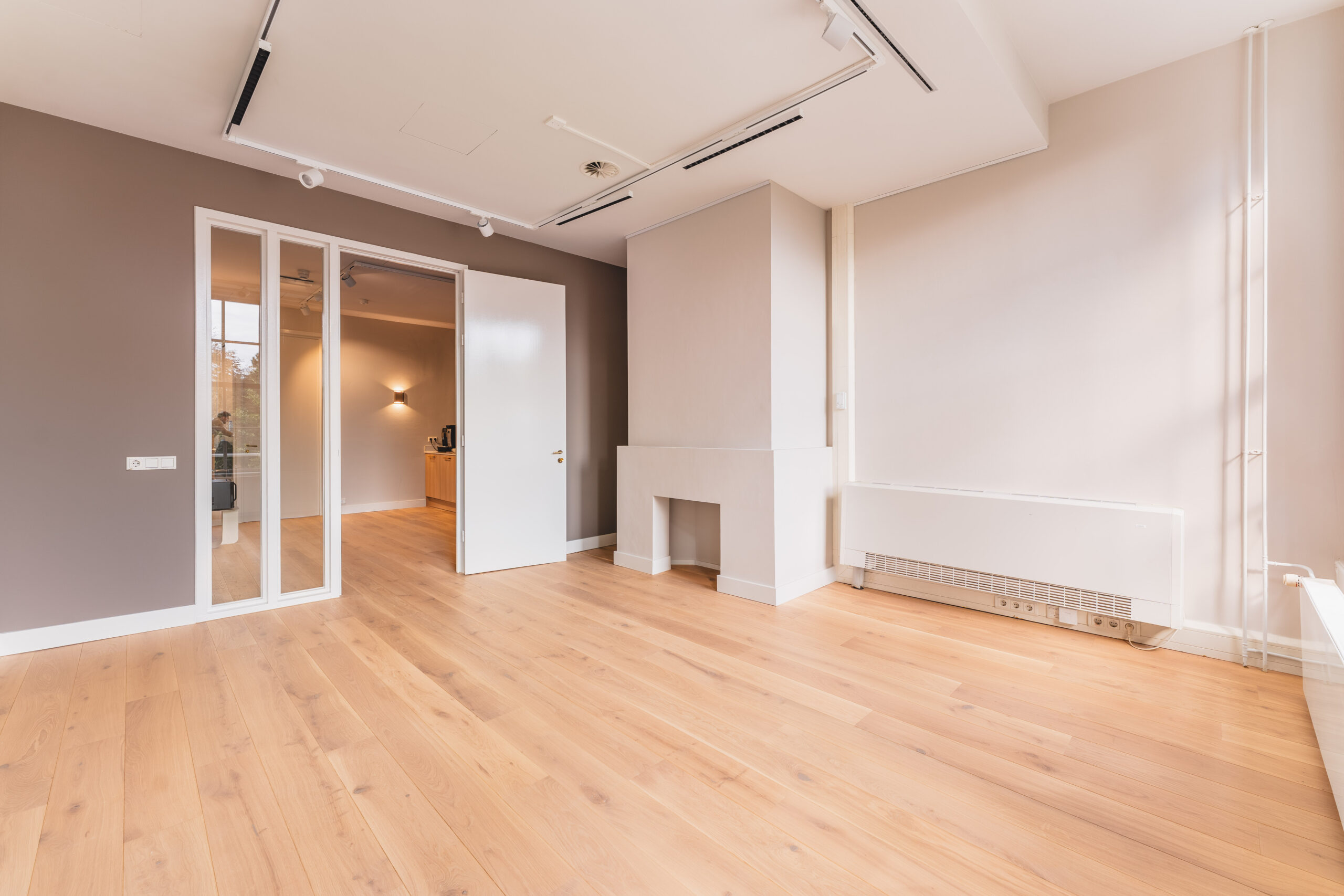 Bright, modern room with wooden flooring, a white radiator, and an open door leading to another space.