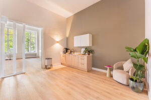 Modern kitchenette with light wood cabinets, a cozy chair, and large windows letting in natural light at Adress_14.