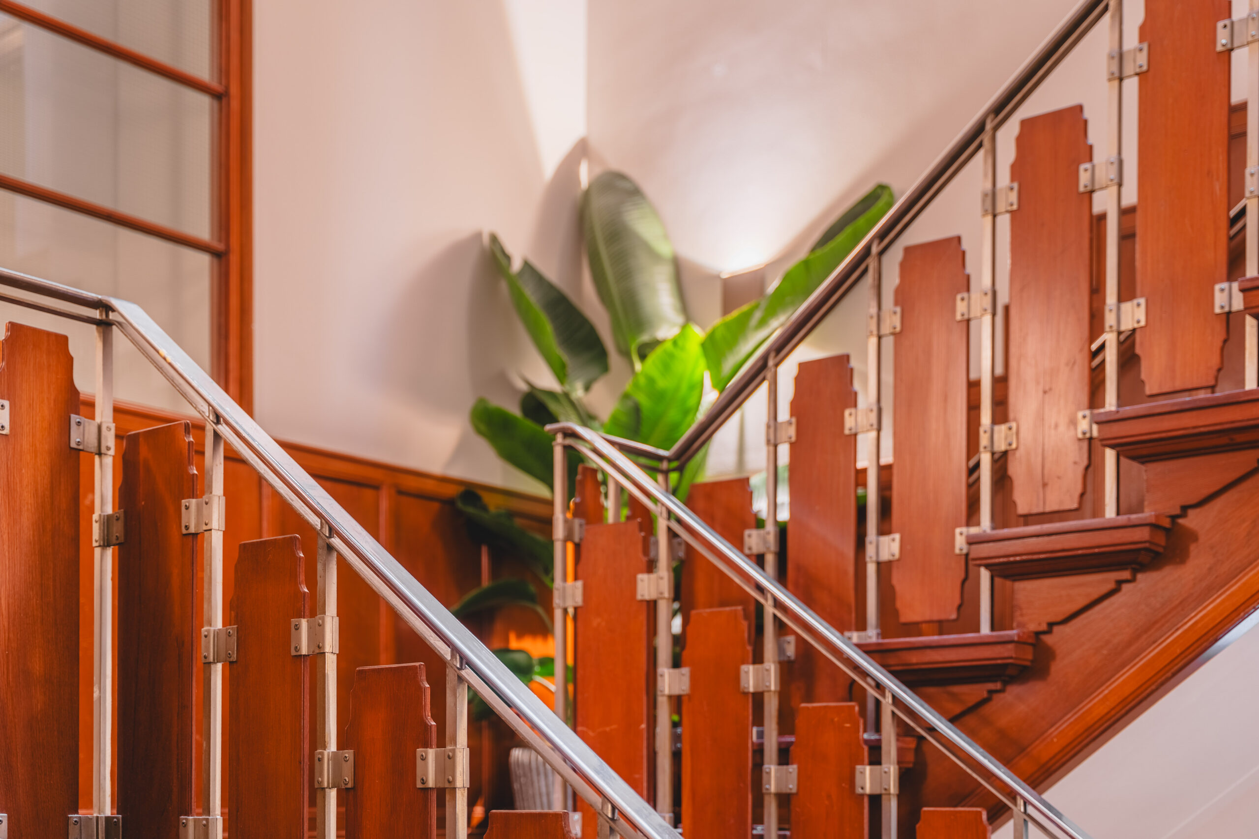 Wooden staircase with geometric railing design and tropical plant in the background at Adress_17.