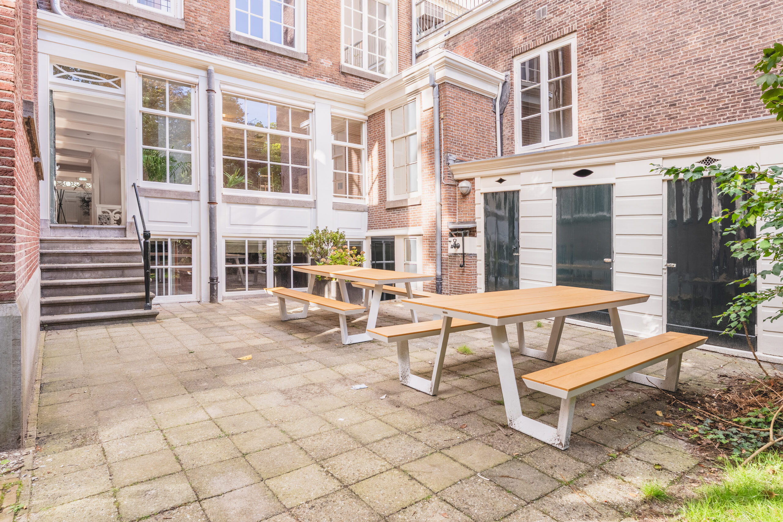 Sunny courtyard of Address_20 with wooden picnic tables and a historic brick facade.