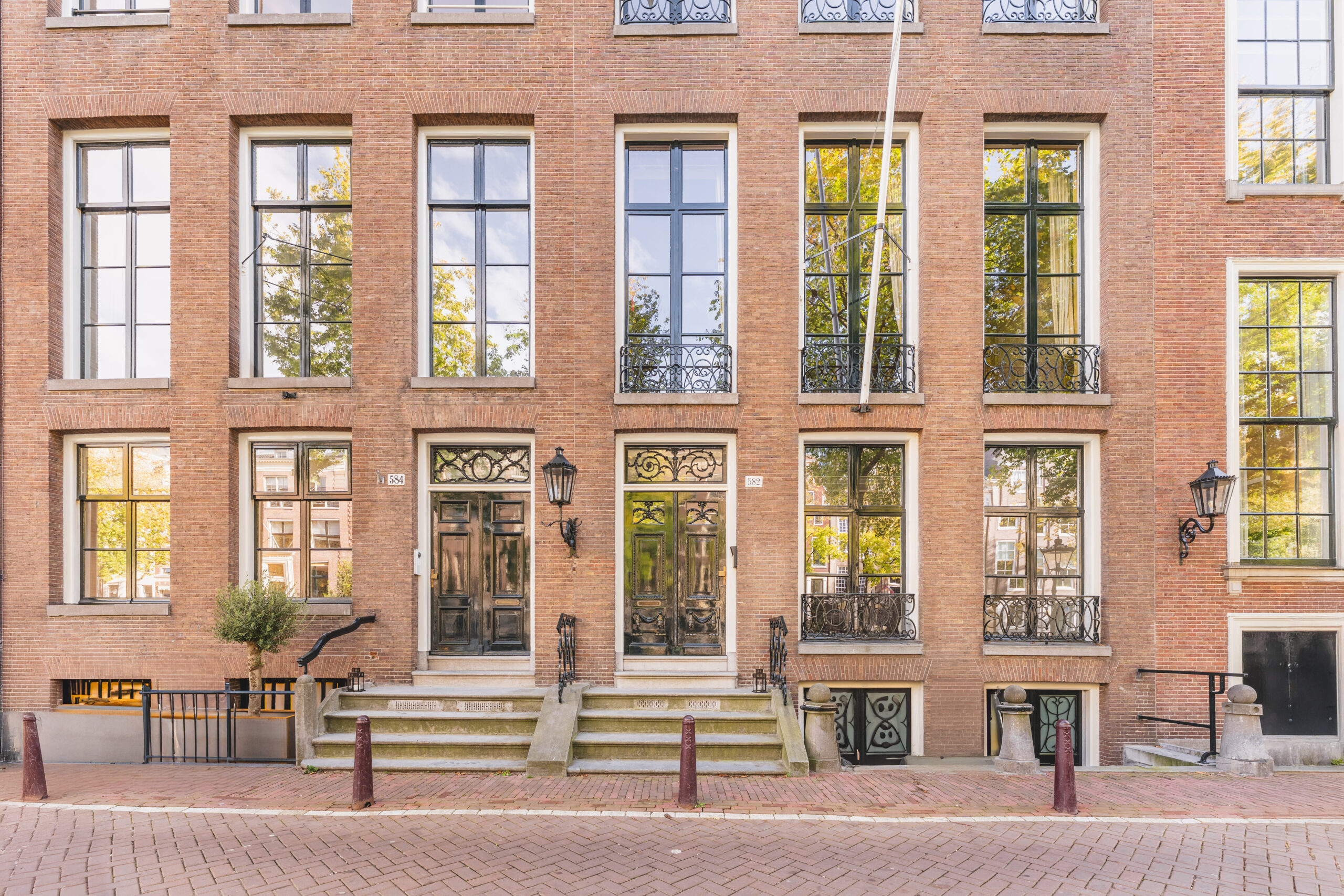 Facade of Adress_21, a historic brick building with large windows and ornate black doors in a canal-side Amsterdam street.