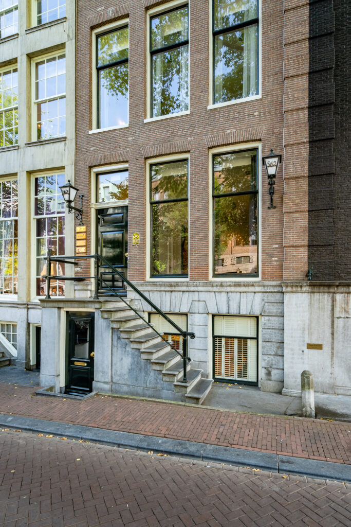 Voorgevel van een Amsterdams grachtenpand met trapgevel, hoge ramen en een toegangstrap naar de voordeur.