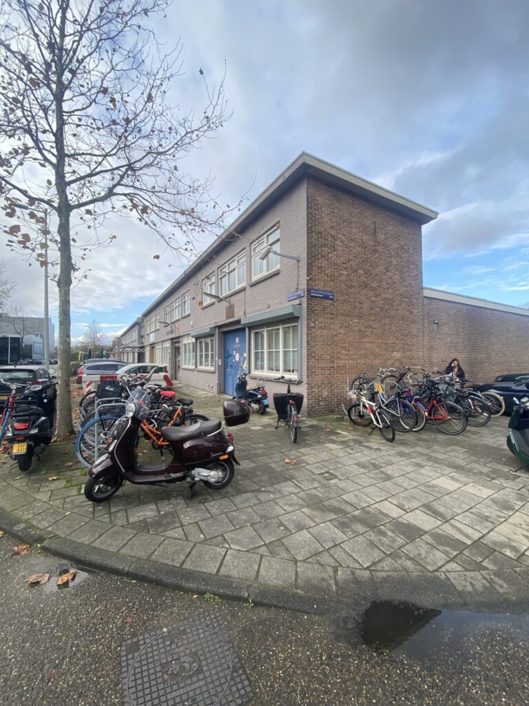 Straathoek met een bakstenen gebouw, geparkeerde fietsen en scooters op de stoep in een woonwijk.