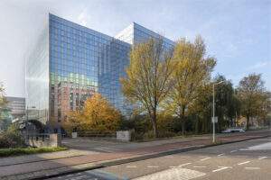 Modern glass office building of MRP Flex Offices surrounded by autumn trees and a quiet street.