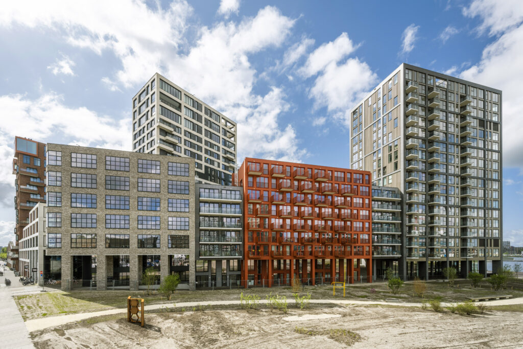 Moderne woongebouwen in het project Southdock, ontworpen door Paul Starink, met opvallende rode en glazen gevels onder een deels bewolkte hemel.
