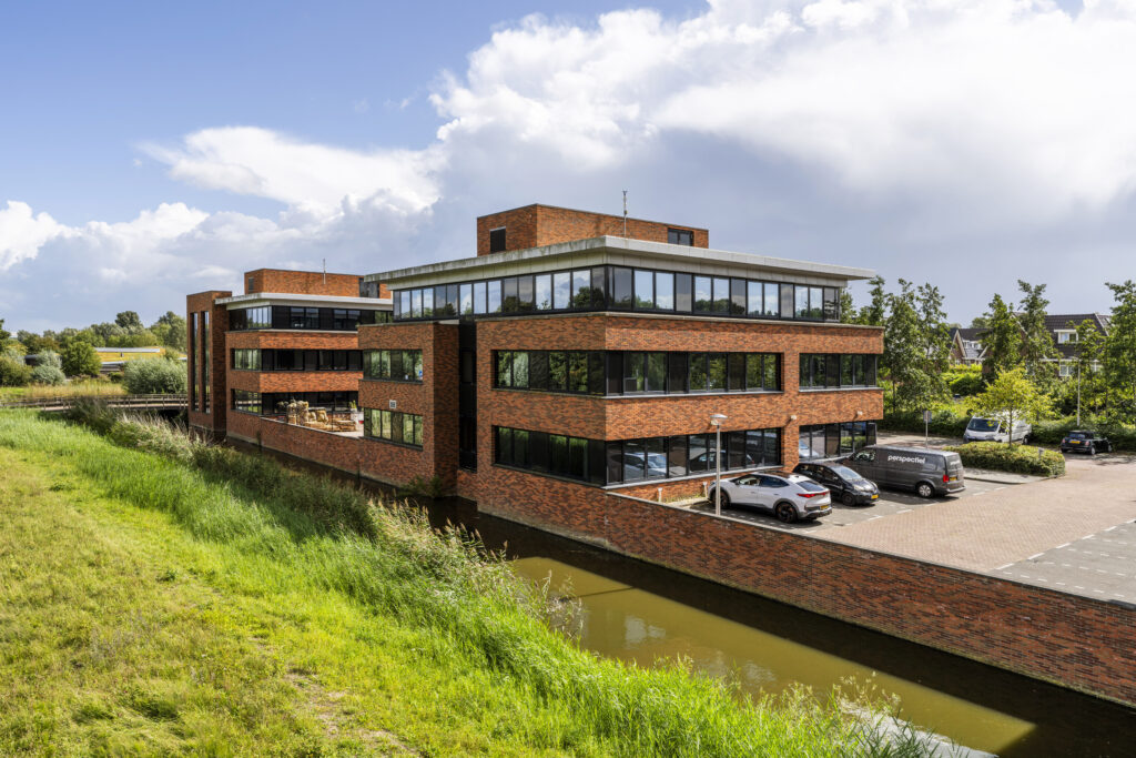 Modern kantoorgebouw aan de Veteranenstraat met bakstenen gevel, parkeervakken en aangrenzende waterpartij.
